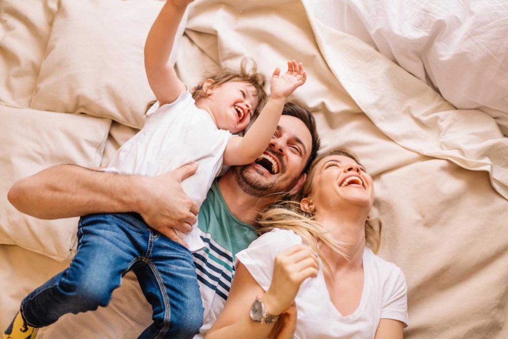 Eine junge Familie mit Mutter, Vater und Kind liegend lachend auf einem Bett.