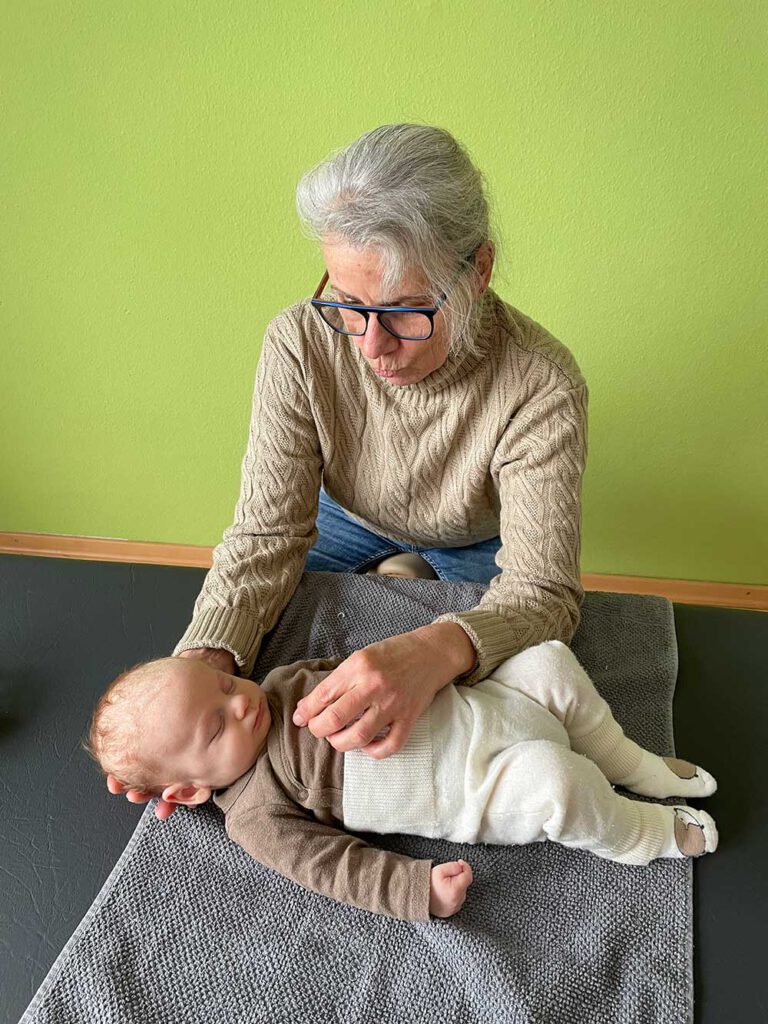 Frau Huss behandelt einen Säugling, der entspannt auf einer Decke liegt.
